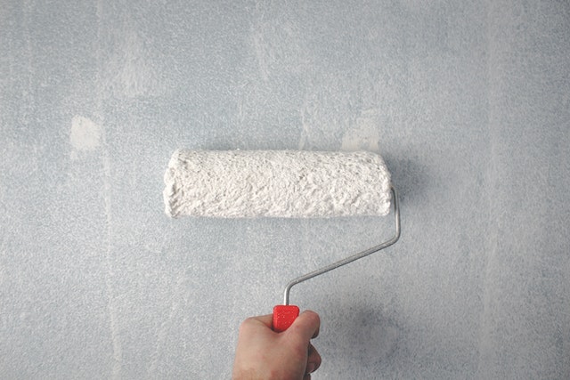 Hand holding a white paint roller on a gray wall