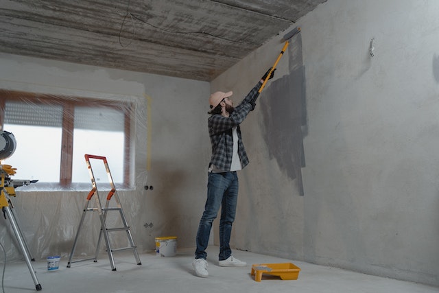 Person painting a wall, surrounded by painting materials
