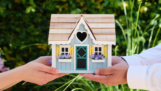 Two pair of hands holding a miniature house