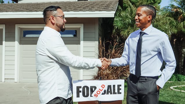 Teo people shaking hands in front of a "Sold" sign on a residential property