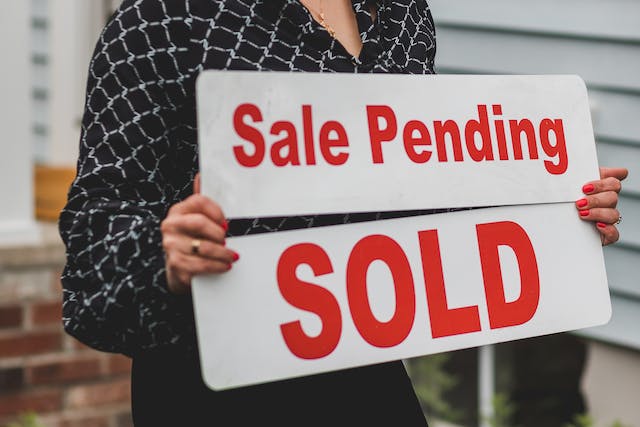 a person holding a sale pending and sold sign in front of a house